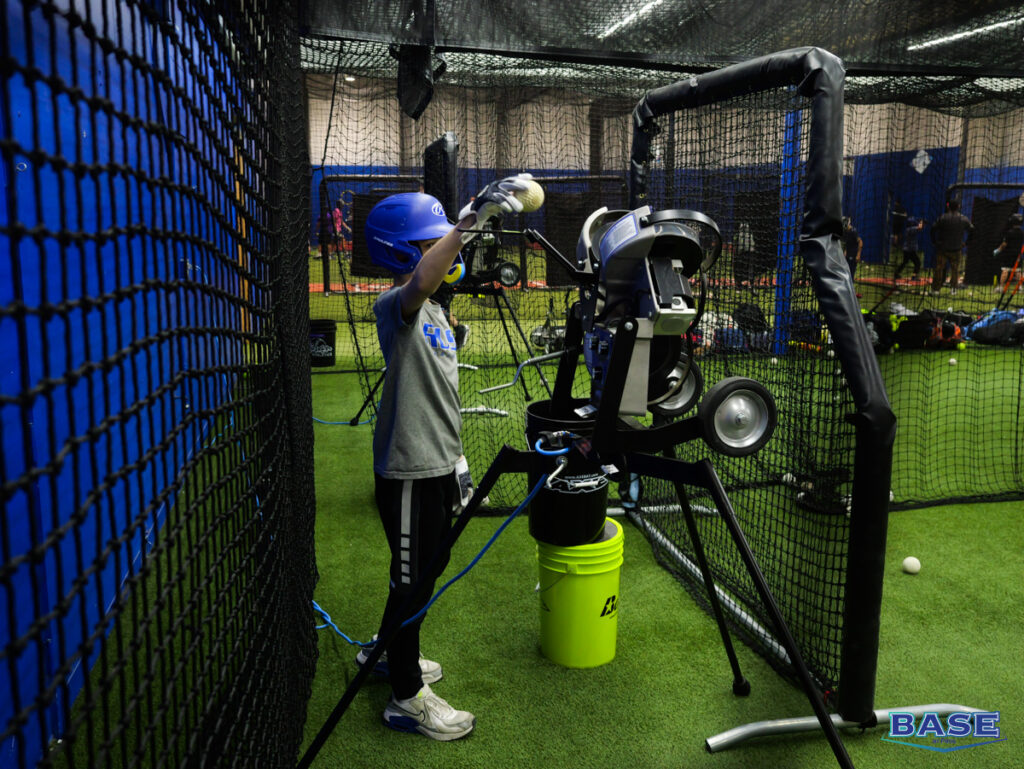 Boy in Blue Helmet Feeds Pitching Machine